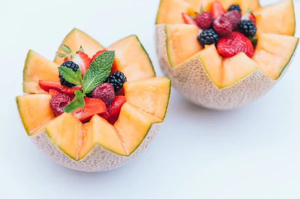 Design de alimentos e conceito de nutrição saudável. Framboesa fresca deliciosa, morango e amora com hortelã em melão esculpido. Cantaloupe com frutas contra fundo branco . — Fotografia de Stock