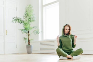 Pozitif kadın kapüşonlu giyer, lotus poz oturur, spor yaptıktan sonra eğlendi, sabah yoga eğitimi, fitness egzersiz, katta modelleri için mutlu, mutlu hissediyor. İnsanlar, enerji, egzersiz kavramı