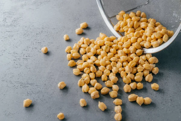 Dry clean chickpeas spilled on grey background from sieve. Food ingredients for vegetarians. Useful seeds. Organic vegan product