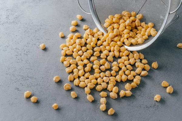 Nutritious dry chickpeas spilled from sieve on grey background. High energy food. Healthy snack. Protein organic product — Stock Photo, Image