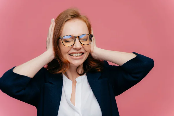 Frustrerad ung affärskvinna har huvudvärk, ignorerar högt brus, täcker öron med händer, knyter tänder, har slutna ögon, bär elegant svart och vitt Formalwear, isolerad på rosa bakgrund — Stockfoto