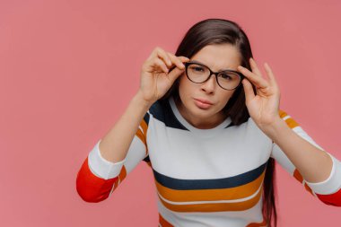 Esmer kadın mesafe içine konsantre, titizlikle toraks optik gözlük görünüyor, jant üzerinde eller tutar, mesafe dikkatli bakışları vardır, küçük harflerle bir şey okumaya çalışır, pembe izole