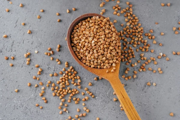 Ungekochter brauner Buchweizen im Kochlöffel vor grauem Hintergrund. Bio-Lebensmittel-Konzept. Buchweizenkörner. Zutaten zum Kochen von Brei — Stockfoto