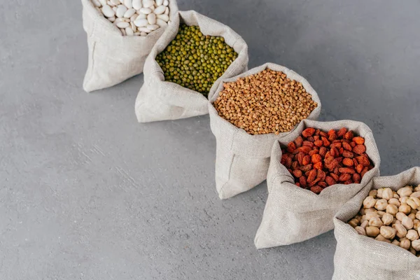 Assorted gluten free grains in linen cloth bags on grey background. Sacks filled with kidney bean, lentil, buckwheat, goji and garbanzo. Cereals for healthy eating — Stock Photo, Image