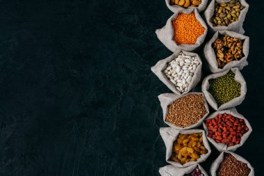 Reklam Için kopya alanı ile siyah arka plan üzerinde izole fasulye tohumu ve kurutulmuş meyve ile dolu küçük çuvallar üst görünümü