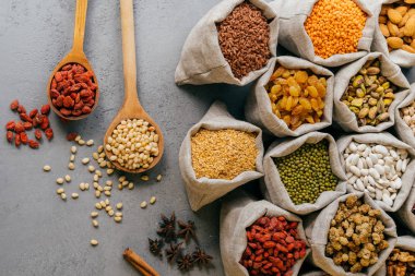 Vejetaryen ürünler. Kuru üzüm, goji, badem, dut ve diğer tahıllar, yıldız anason yakın, iki tahta kaşık dolu küçük hessian çuvalüst düz görünümü