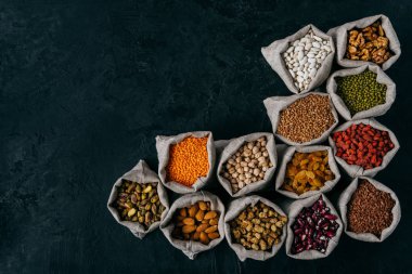 Badem, ceviz, kuru üzüm, garbanzo, böbrek fasulyesi, kırmızı goji, koyu arka plan üzerinde izole, reklam için boş alan ile dolu küçük çuvalyatay çekim