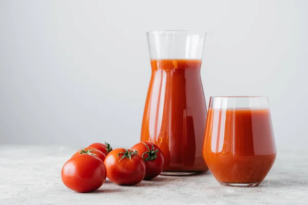 Raw tomatoes and glass of freshly drink, isolated over white background. Tomato juice made of vegetables in transparent glasses. Healthy drink — Stock Photo, Image