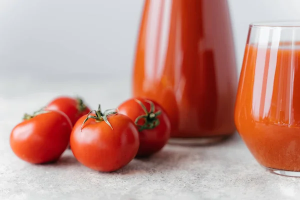 Tomatensaft in zwei Glasbechern und kleine reife rote Tomaten auf weißem Hintergrund. frisches Getränk mit Vitaminen. gesunde Ernährung — Stockfoto