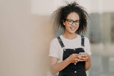 Gülümseyen genç Afro kadınlar modern cep telefonlarına sahipler, mobil uygulama kullanıyorlar, modern teknolojilerin dünyasında yaşıyorlar, sosyal ağlara bağımlılar, çevrimiçi arkadaşlarla sohbet ediyorlar, şık kıyafetler giyiyorlar.