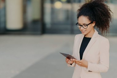 İşletme şirketinin başarılı sahibi ekranda dijital touchpad 'le ayakta duruyor, piyasanın gelişmesi için yeni fikirler arıyor, gözlük takıyor ve beyaz resmi ceket giyiyor. İş kadını dışarıda.