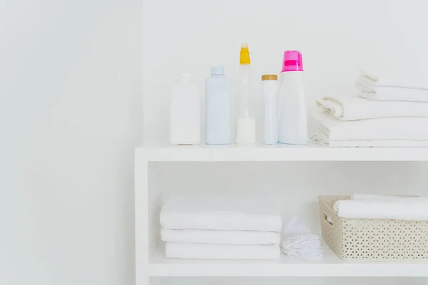 Stack of clean white towels with detergents on console isolated over white background. Fresh laundry and liquid washing in bathroom — Stock Photo, Image