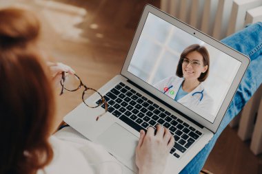 Tanınmayan bir kadın, laptopta deneyimli bir doktorla görüntülü konuşma yapıyor. Karantina sırasında danışmanlık alıyor. Hastalık tedavisini tartışıyorlar. Pratisyen hekimle görüntülü konuşma. Arka arkaplan