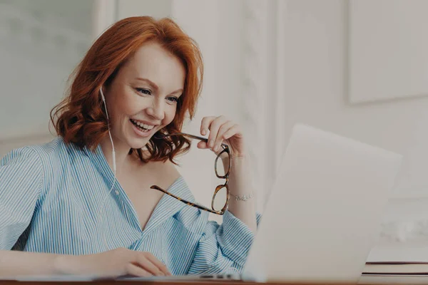 正の赤毛の実業家は オンライン会議に参加し ノートパソコンの表示に焦点を当てた家庭教師とトレーニングクラスを持っている 眼鏡を保持し 教育のウェビナーを見て楽しんでいます — ストック写真