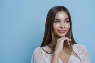 Güzel bir kadının portresi çeneye dokunuyor ve düşünceli bir ifade takınıyor, başka yere bakıyor, mavi arka planda izole edilmiş, reklamınız ya da terfiniz için boş bir alan. Romantizm ve güzellik kavramı