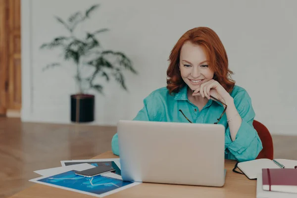赤い髪の仕事や現代のラップトップコンピュータ上の研究で千年紀の女性を笑顔 インターネットを閲覧 ビデオ会議を持っています クライアントにオンライン相談を与えます 仕事の昇進や素敵なオファーを取得 — ストック写真