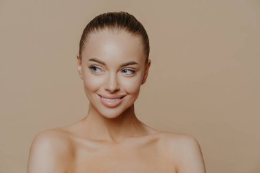 Temiz ciltli, doğal makyajlı ve bej arka planda beyaz dişli güzel bir kız. Moda, güzellik, makyaj, kozmetik.