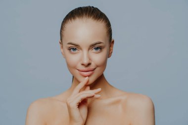 Saf ve sağlıklı tenli hassas bir kadın, doğal bir çekiciliği var, kendini güzel ve çekici hissediyor, mavi arka planda üstsüz duruyor, spa ameliyatlarından sonra keyfine bakıyor. Güzellik bakımı