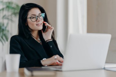 Ciddi iş kadınlarının telefonda konuştuğu, dizüstü bilgisayarın önünde poz verdiği, görüş düzeltmesi için optik gözlük taktığı, iş yerinde poz verdiği, resmi olarak giyindiği,