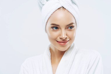 Spa, güzellik ve tazelik konsepti. Düşünceli, sağlıklı tenli, düşünceli bir Avrupalı kadın banyo prosedürlerinden sonra kendini yenilenmiş hissediyor, sabahlık giymiş, kafasında havlu var.