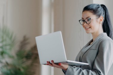 Çalışan şirket çalışanlarının kapalı çekimleri, modern dizüstü bilgisayarı tutuyor, tarihi iletiyor, kablosuz internete bağlanıyor, görsel düzeltme için gözlük takıyor, geri bildirim gönderiyor.