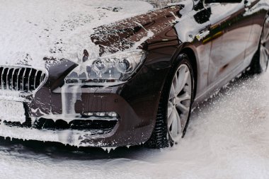 Lavaboda servis edilen siyah arabanın fotoğrafı. Araba yıkamada sabunla kaplı kirli bir otomobil. Profesyonel araba yıkama. Araç temizleme