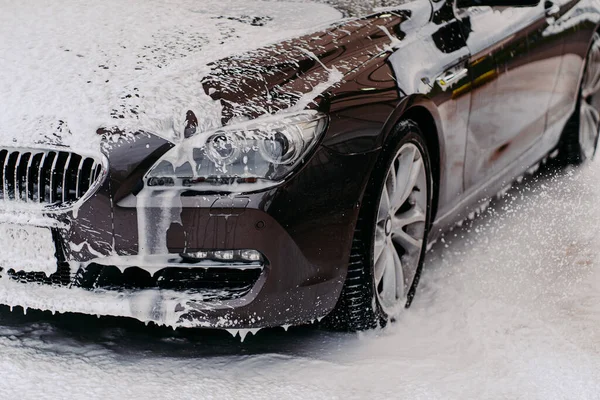 Lavaboda servis edilen siyah arabanın fotoğrafı. Araba yıkamada sabunla kaplı kirli bir otomobil. Profesyonel araba yıkama. Araç temizleme