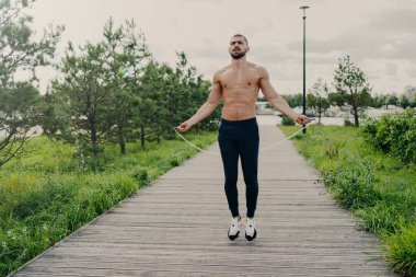Sportif kaslı adam dışarıda kardiyo eğitimi için ip atlıyor. Mükemmel bir vücudu var. Temiz hava soluyor ve dayanıklılık gösteriyor. Spor ekipmanlı bir sporcu.
