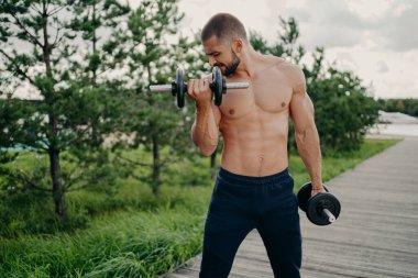 Halterle hareket eden kaslı adamın yatay pozu erkekliğin güçlü bir vücut gücü olduğunu gösterir. Üstsüz durmak, ağırlık kaldırmak için çabalamak, bisepslerin kıvrımlarını yapar.