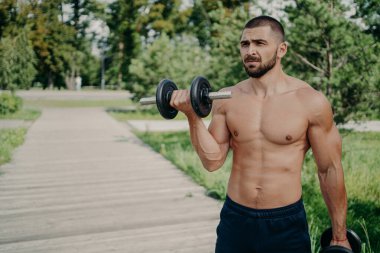 Üstsüz halterci ağır haltercileri kaldırır, güçlü halterleri sever, sağlıklı yaşam tarzına sahiptir, mesafeye odaklanır, dışarıda egzersiz yapar, dambılı kaldırır, fiziksel olarak iyi durumdadır. Spor konsepti