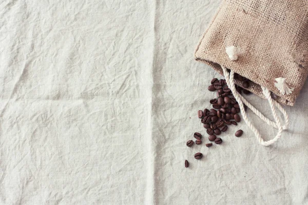 Coffee beans in bag on linen tablecloth. Top view. Copy space