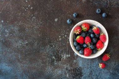 Grunge taş zemin üzerine seramik tabak taze yaz meyveleri (yaban mersini, çilek, ahududu). Üstten görünüm. Kopya alanı