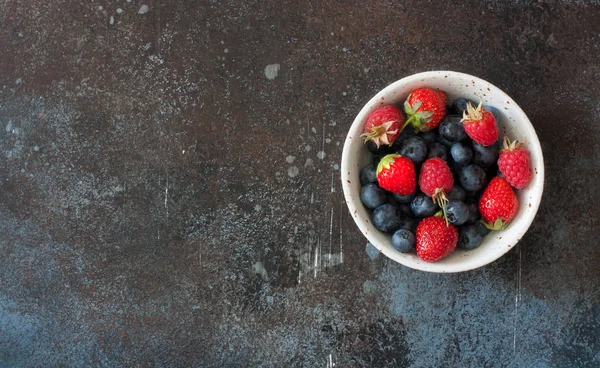 Grunge taş zemin üzerine seramik tabak taze yaz meyveleri (yaban mersini, çilek, ahududu). Üstten görünüm. Kopya alanı   