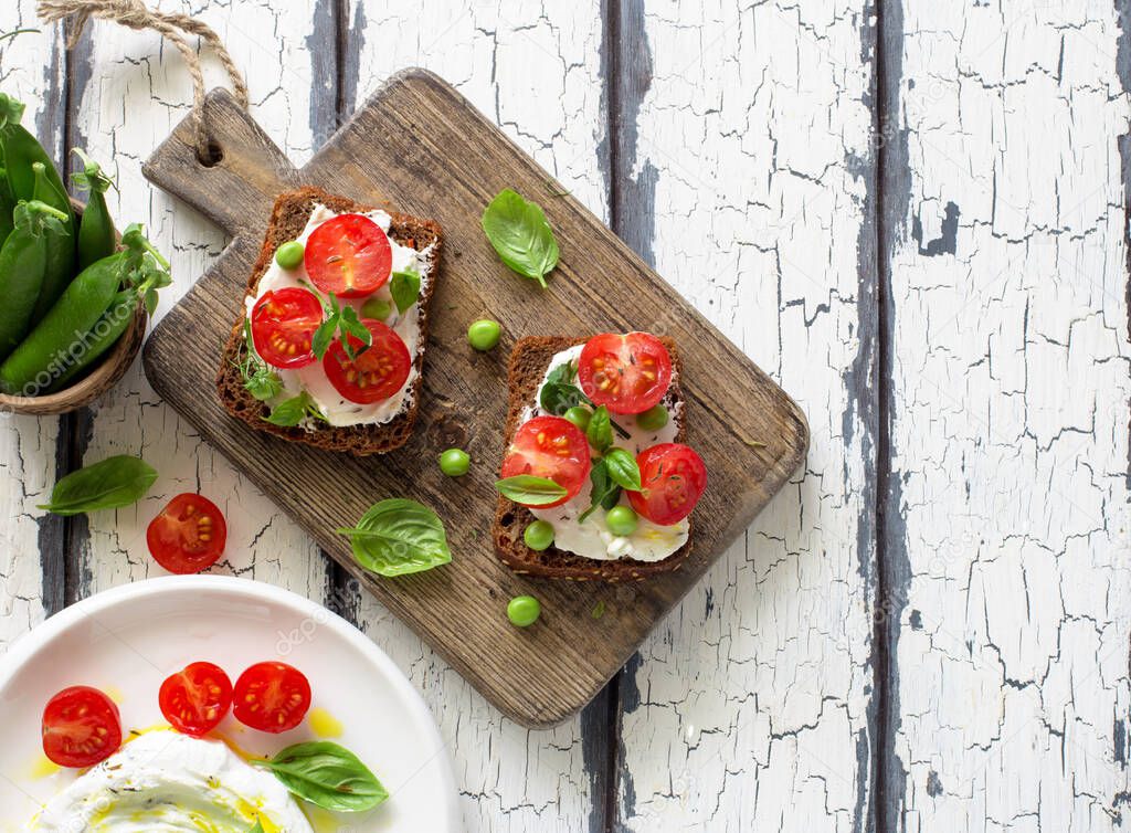 Open sandwiches with cream cheese,cherry tomatoes, green peas and basil close up. Flat lay