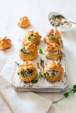 Krem peynirle doldurulmuş profiteroller ve beyaz tahta arka planda mantarlar. Düz yatıyordu