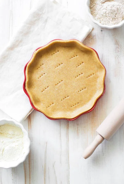 Crust on baking sheet , pots with wheat and bran flour and rolling pin on white wooden table. Flat lay. Copy space