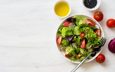 Beyaz ahşap arka planda yeşil yapraklar, domatesler, avokado ve salatalık salatası. Düz yatıyordu. Boşluğu kopyala