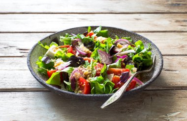 Doğal ahşap zemin üzerinde taze yeşil yapraklar, domatesler, yumuşak peynir ve ceviz salatası. Kapat.