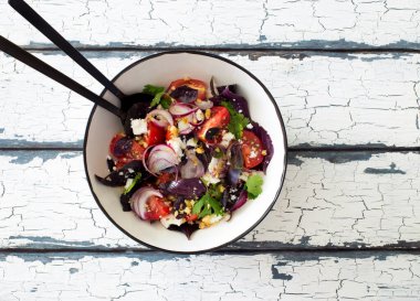 Beyaz kasede taze yeşil yapraklar, domatesler, yumuşak peynir ve ceviz salatası. Düz yatıyordu