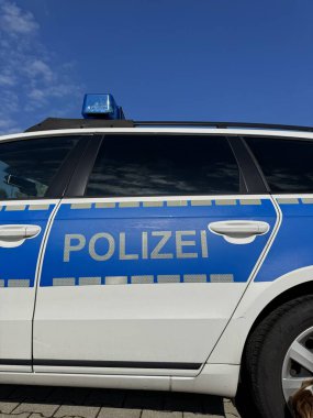 A police car featuring a distinct blue and white design is parked beneath a clear and bright blue sky above