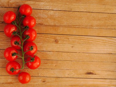 Bir grup kırmızı domates ahşap bir masanın üzerinde. Domatesler sıraya dizilir, bazıları birbiriyle çakışır. Görüntünün basit ve doğal bir havası var, taze olan üzerine odaklanarak.