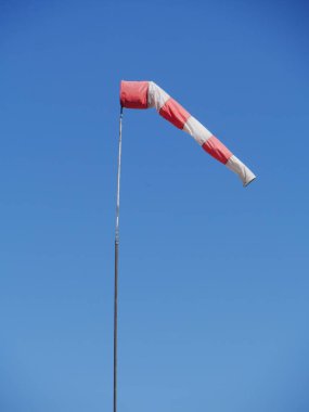 Kırmızı ve beyaz çizgili uçurtma gökyüzünde uçuyor. Uçurtma bir direğe bağlı ve sağ tarafı gösteriyor. Gökyüzü açık ve mavi, ve rüzgar yok.