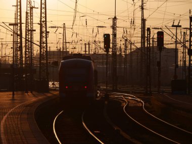 Train is traveling down a track in the evening. The train is surrounded by many electrical wires and lights. Scene is calm and peaceful, as the train moves through the quiet countryside