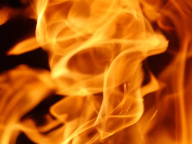 Bu resim turuncu ve sarı renkli bir alevin görüntüsü. Alev çok büyük ve içinden çok fazla duman çıkıyor. Sahne yoğun ve dramatik.