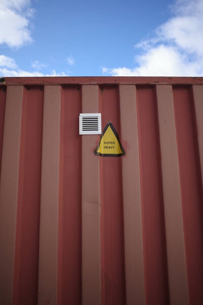 Red container with a yellow sign on it that says "No Entry" is on a red wall. The container is likely used for storing hazardous materials or other dangerous items