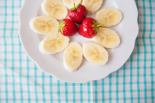 Banana e morangos em um prato branco e um guardanapo colorido — Fotografia de Stock