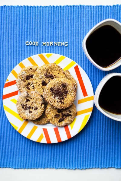 Biscuits à l'avoine avec chocolat sur une serviette bleue et deux tasses de café, inscription bonjour — Photo