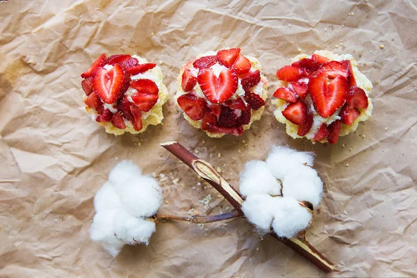 Schöne Cupcakes mit Erdbeeren zusammen mit einem Zweig Baumwolle liegt auf Kraftpapier — Stockfoto