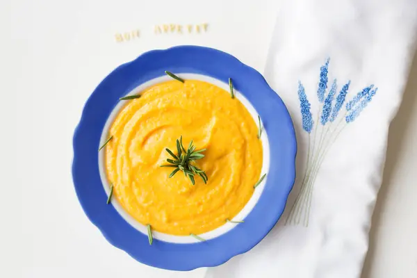 Pumpkin soup in a blue plate on a napkin with flowers — Stock Photo, Image