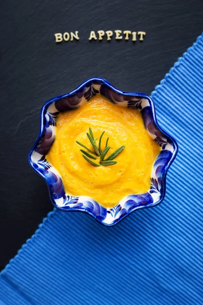 Pumpkin soup in a blue plate on a black background with a blue cloth, close-up — Stock Photo, Image